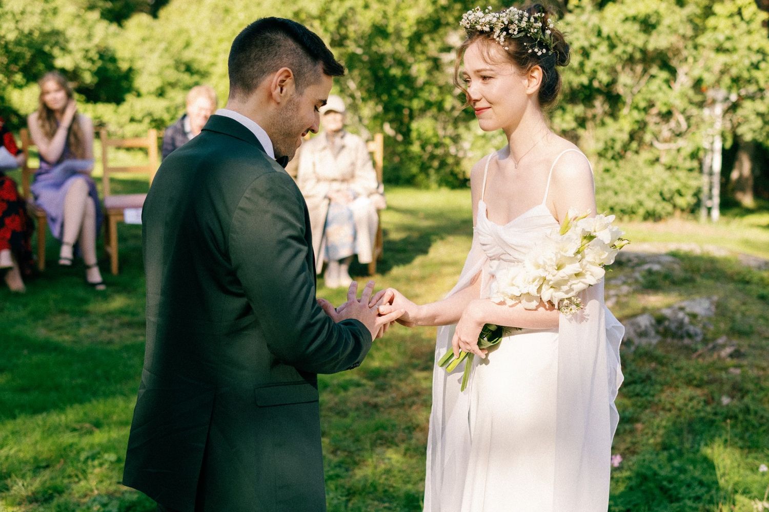 Romantic wedding moment captured on sunny lawn with historic yellow building in background.