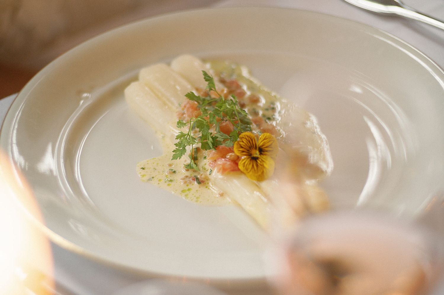 Plated white dish garnished with microgreens and edible flowers in fine dining presentation.