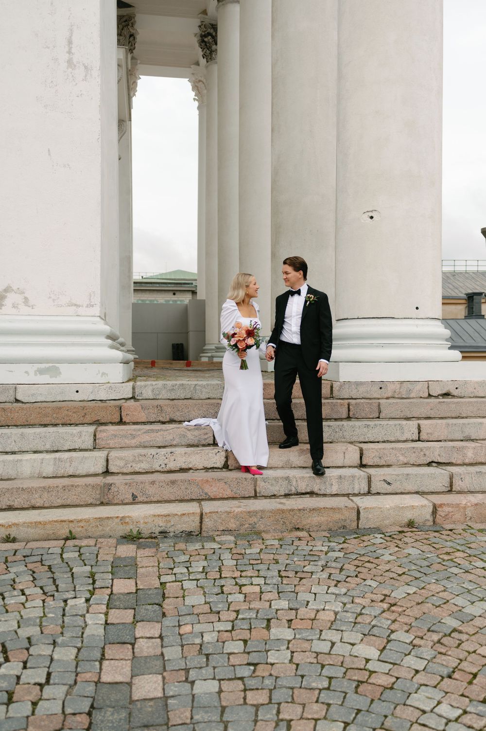 Wedding portrait with couple standing on stone steps against white classical architecture.