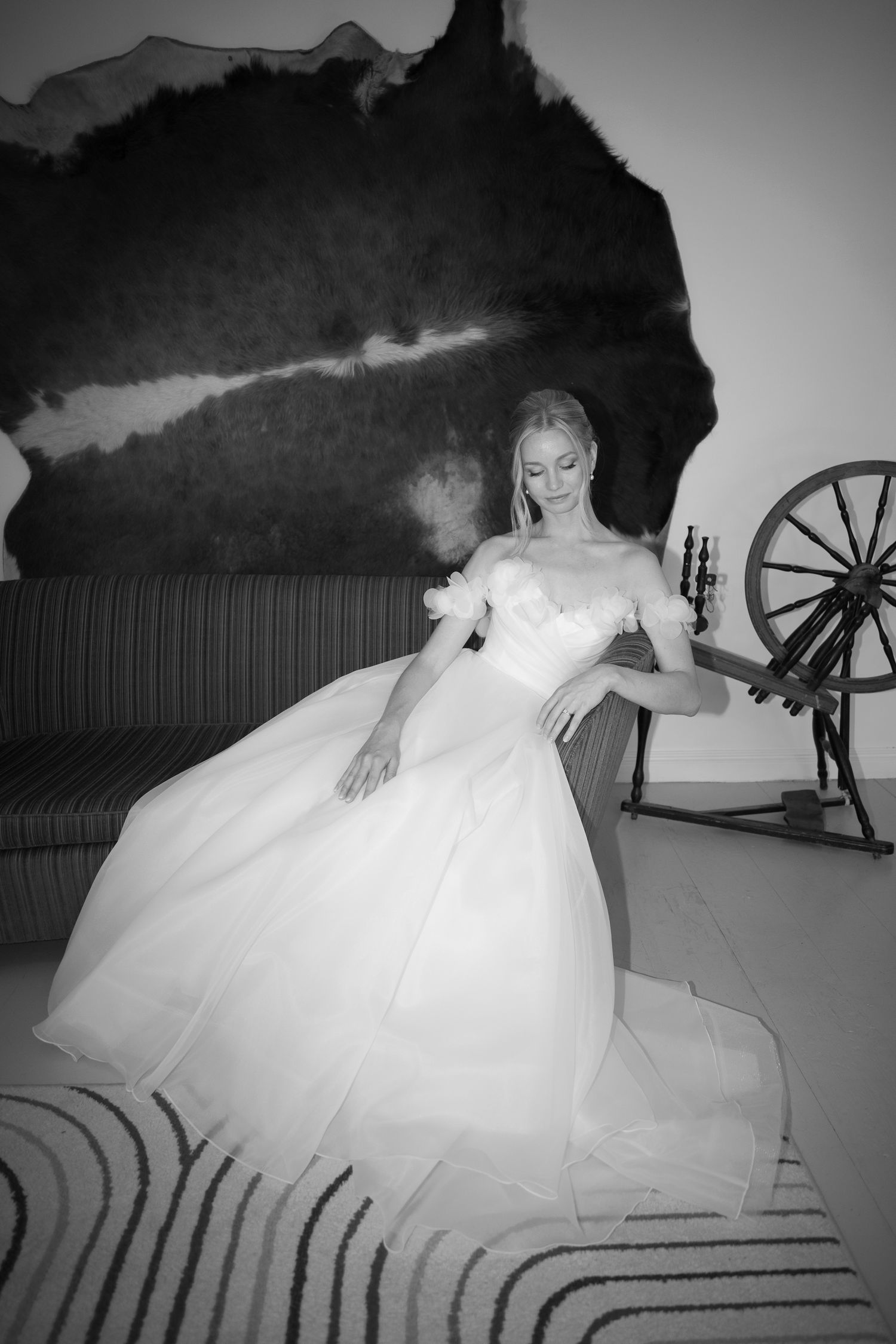 Black and white photo of a bride in a voluminous ball gown sitting gracefully near a vintage spinning wheel.