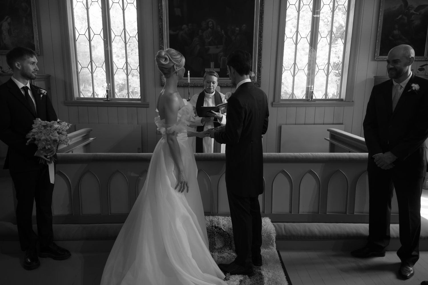 Black and white photo of a bride and groom exchanging vows at a church altar with an officiant.