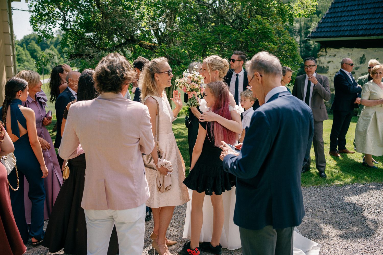 Guests mingling outdoors at a summer wedding reception, with a bride holding a bouquet surrounded by elegantly dressed attendees.