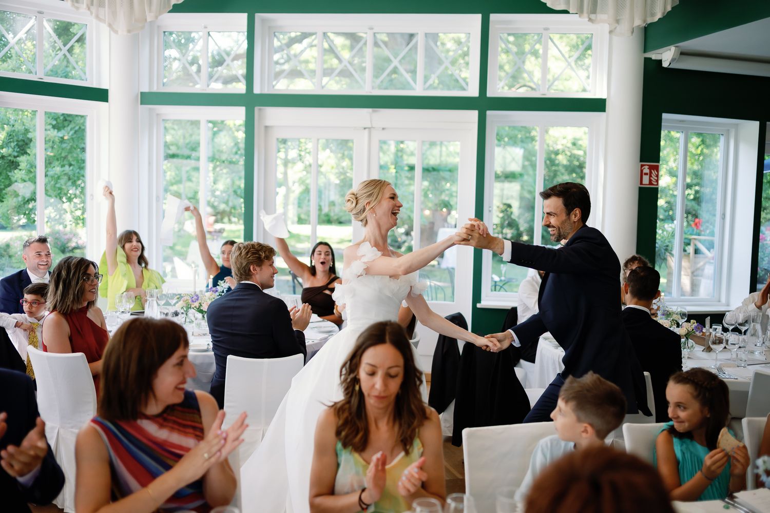 Bride and groom dancing joyfully at wedding reception while guests clap and celebrate in elegant venue.