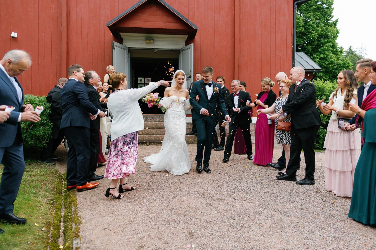 Wedding party and guests line up outside red church building for post-ceremony celebrations.
