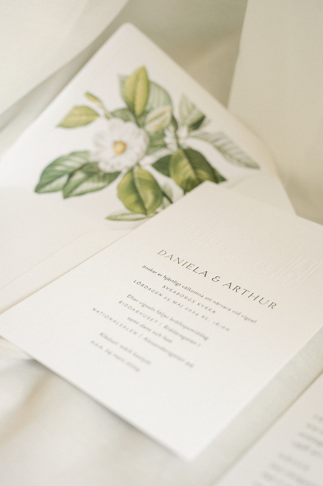 Elegant wedding invitation with watercolor floral design featuring white flowers and green leaves.