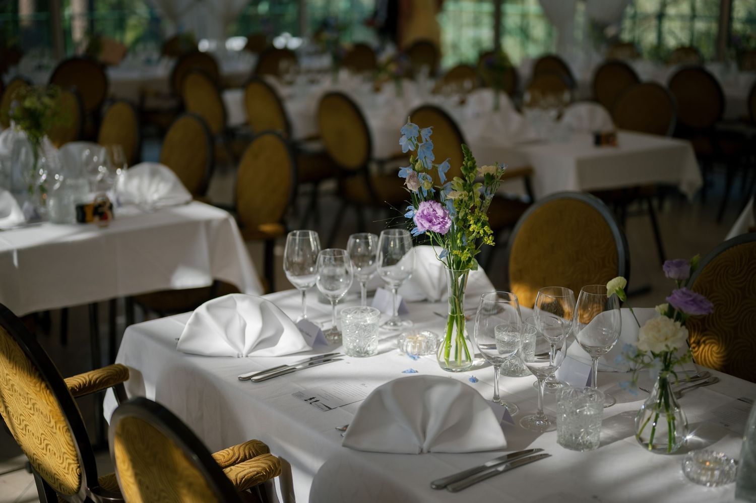 Elegant wedding reception table setting with white linens, wine glasses and delicate floral centerpieces.