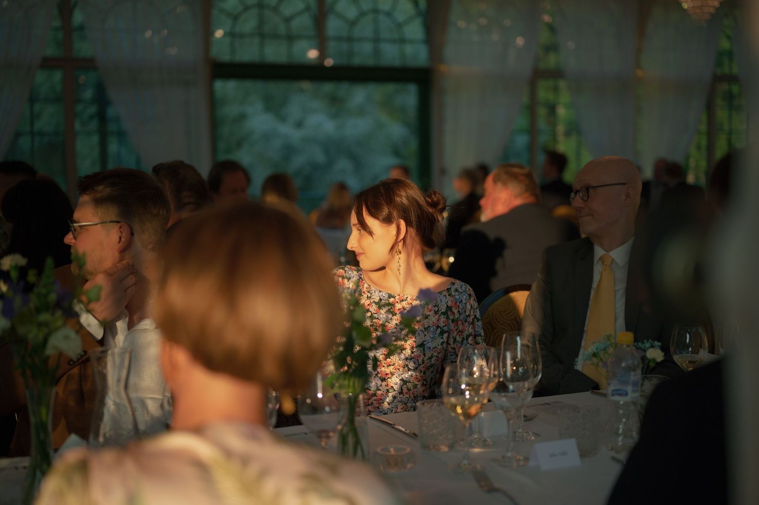 Panoramic view of wedding guests dining at tables in a dimly lit reception venue.