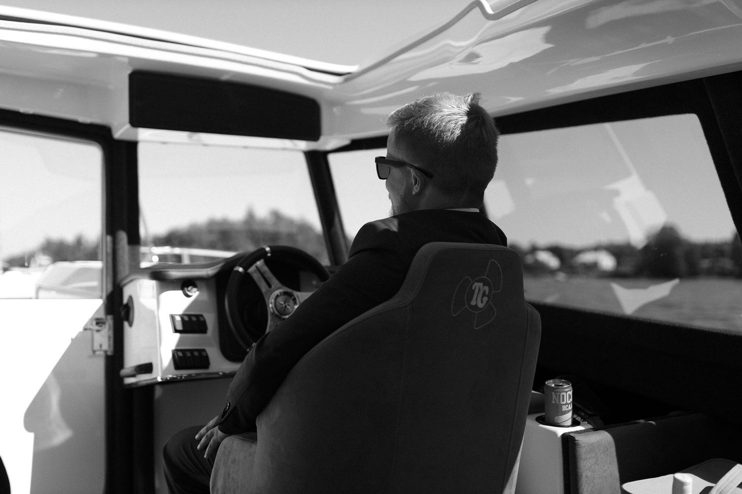 Black and white photo of someone steering a boat across the water.