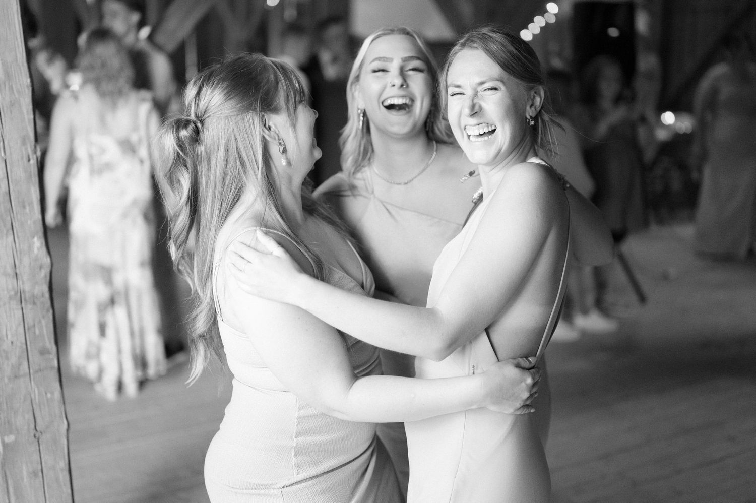 Three women in white dresses share a joyful moment dancing together at a wedding reception.