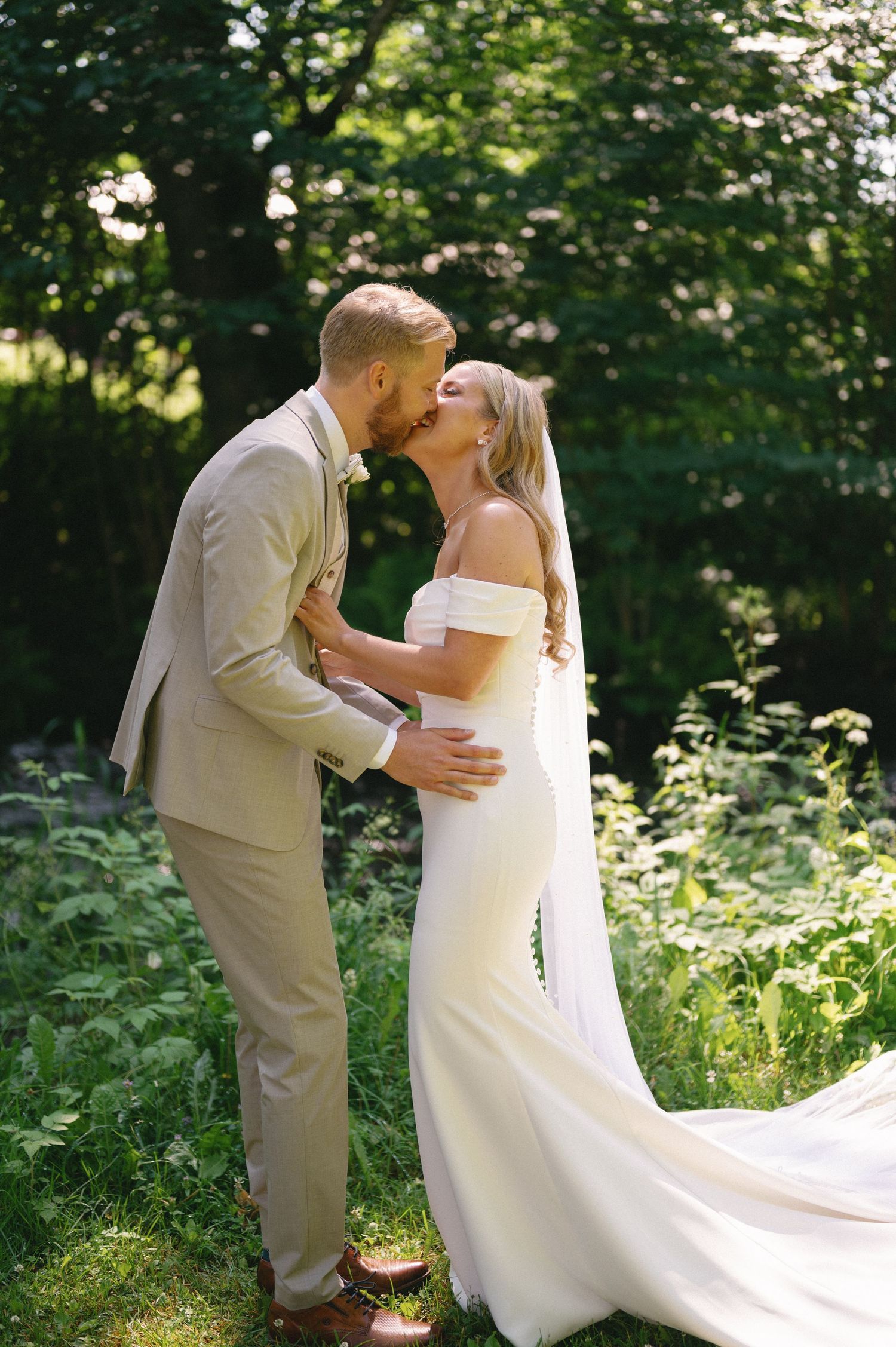 Newlyweds share romantic kisses in a lush garden setting during their wedding photo session.
