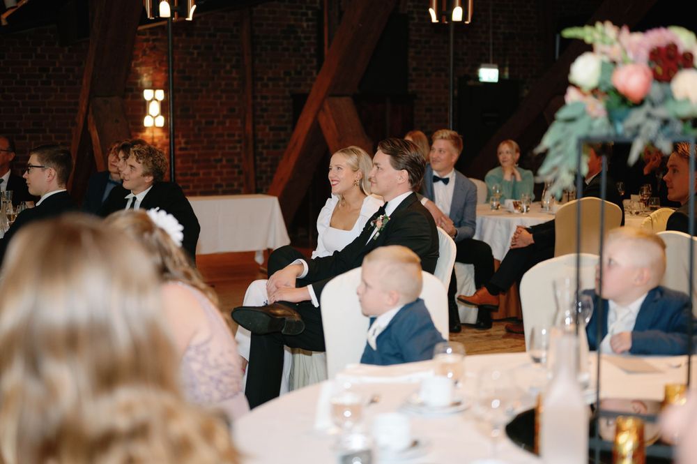 Guests seated at decorated tables during a formal event in a brick-walled venue.