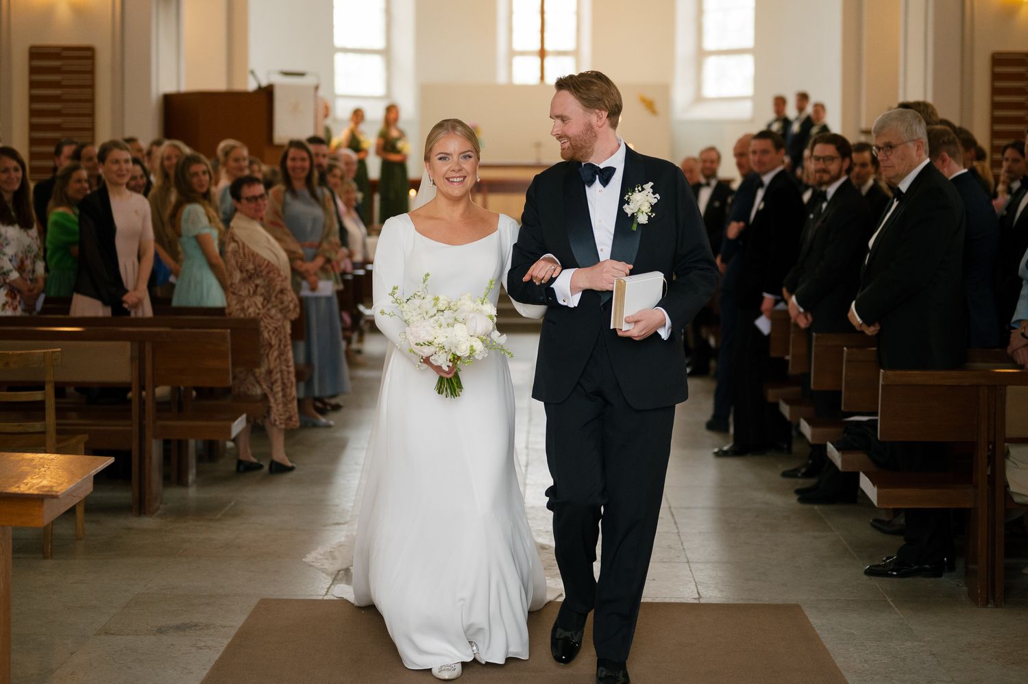 A couple walks down the church aisle together after their wedding ceremony as guests look on from the pews.