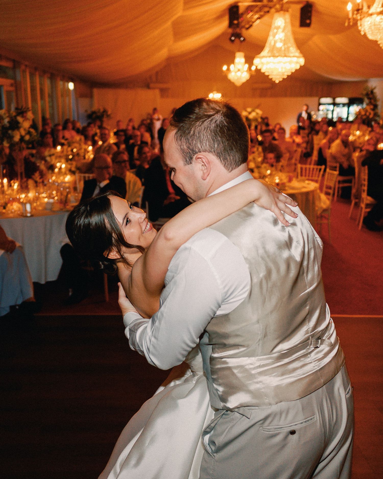 Bride and groom share their first dance under crystal chandeliers at an elegant wedding reception.