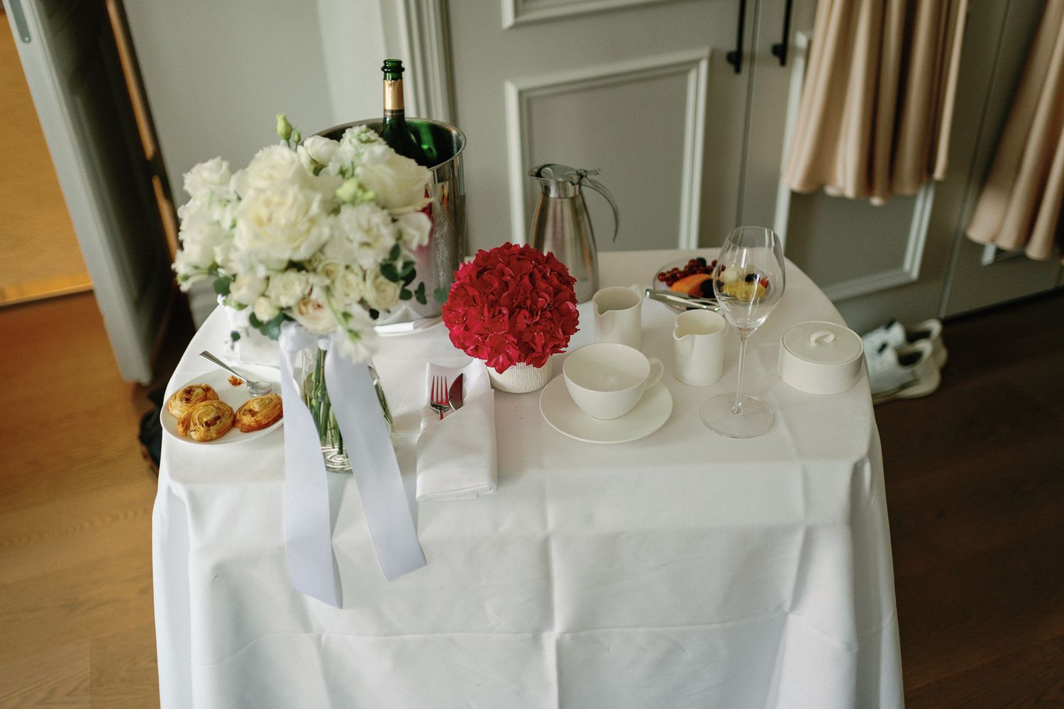 Elegant wedding reception table with white linen, red and white floral arrangements, champagne on ice, and decorative tableware.