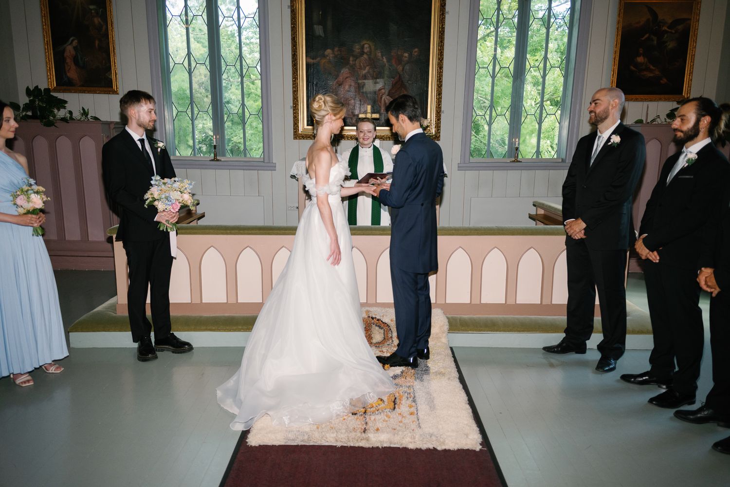 Bride and groom exchanging vows at elegant church altar, surrounded by bridesmaids and groomsmen during wedding ceremony.