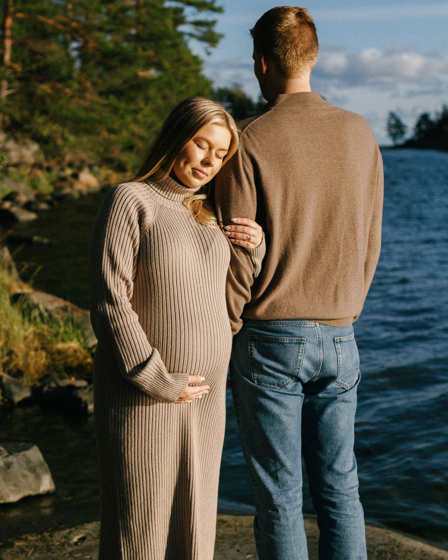 A couple stands by a lakeside wearing cozy sweaters on an autumn day.