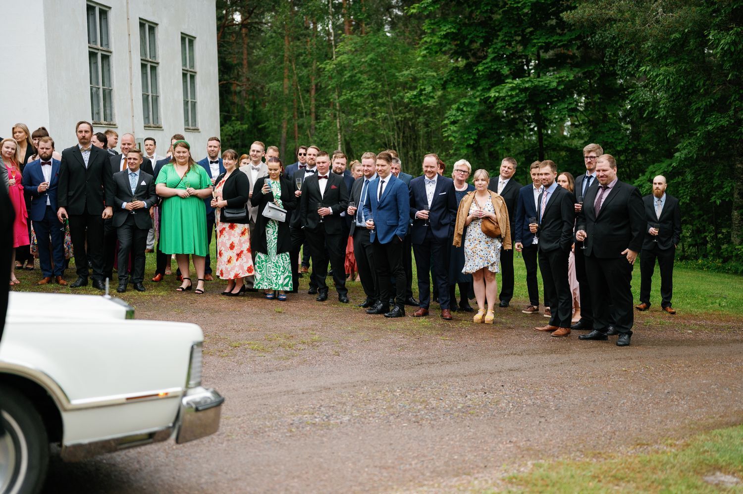 Large group of wedding guests lined up outside a white building for a formal photo.