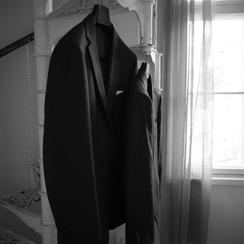 Dark formal suits hanging in a bright white room with natural window light.