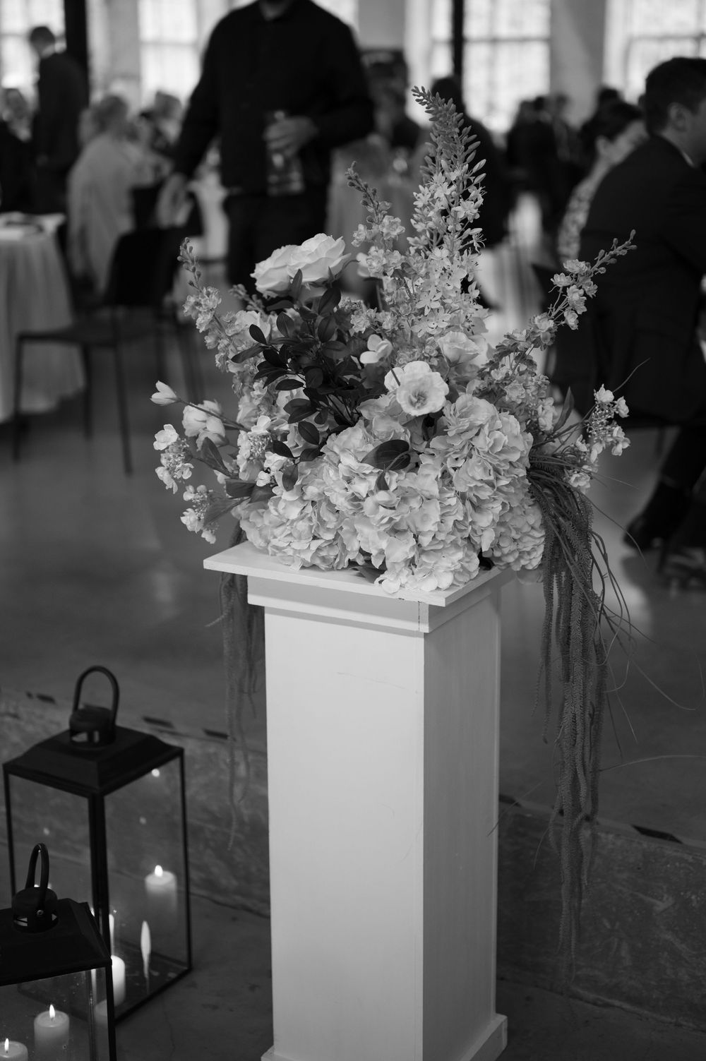 Black and white image of elegant floral arrangements and lanterns at a wedding reception.