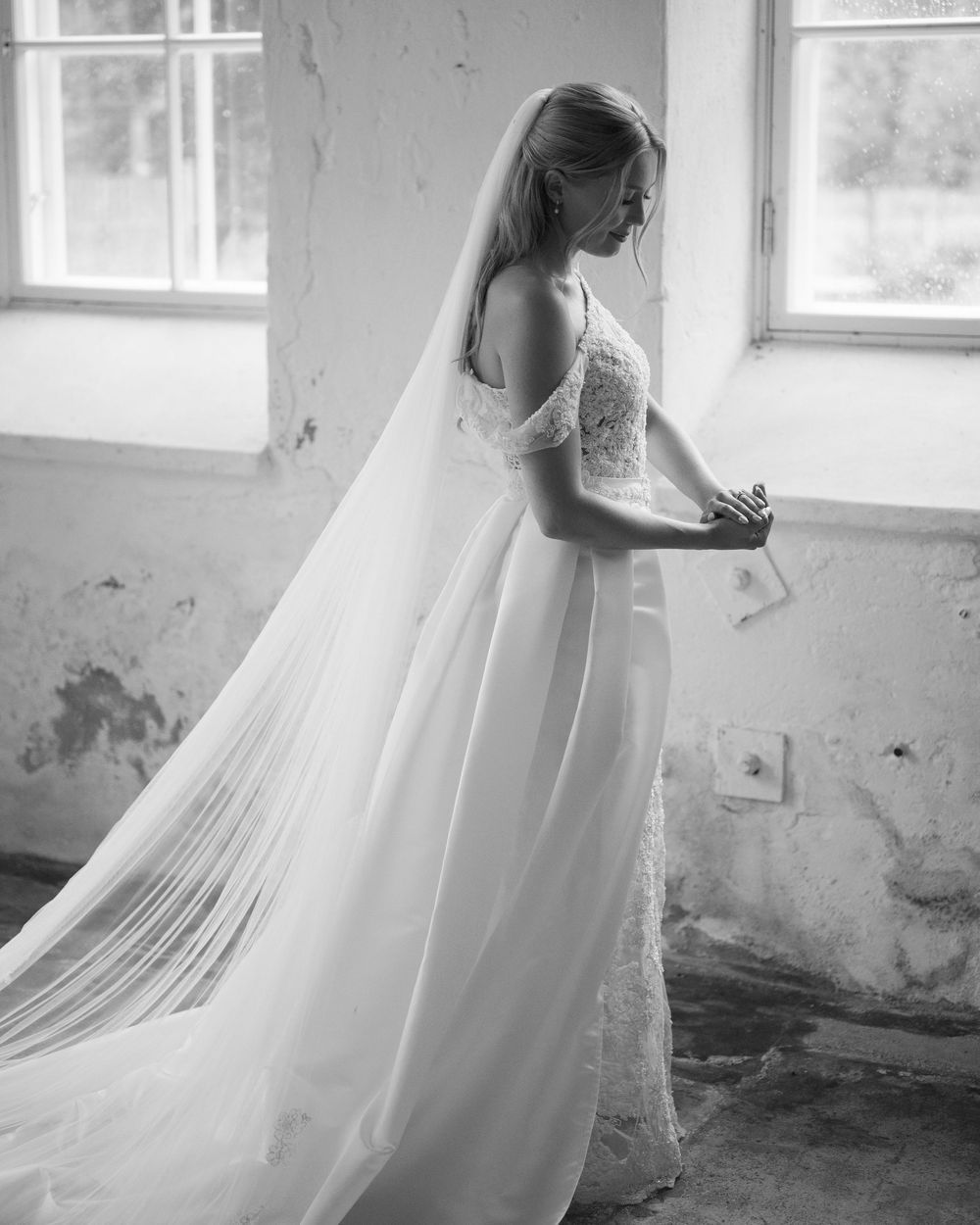 Ethereal bridal portrait with flowing tulle veil in rustic room with natural window light.