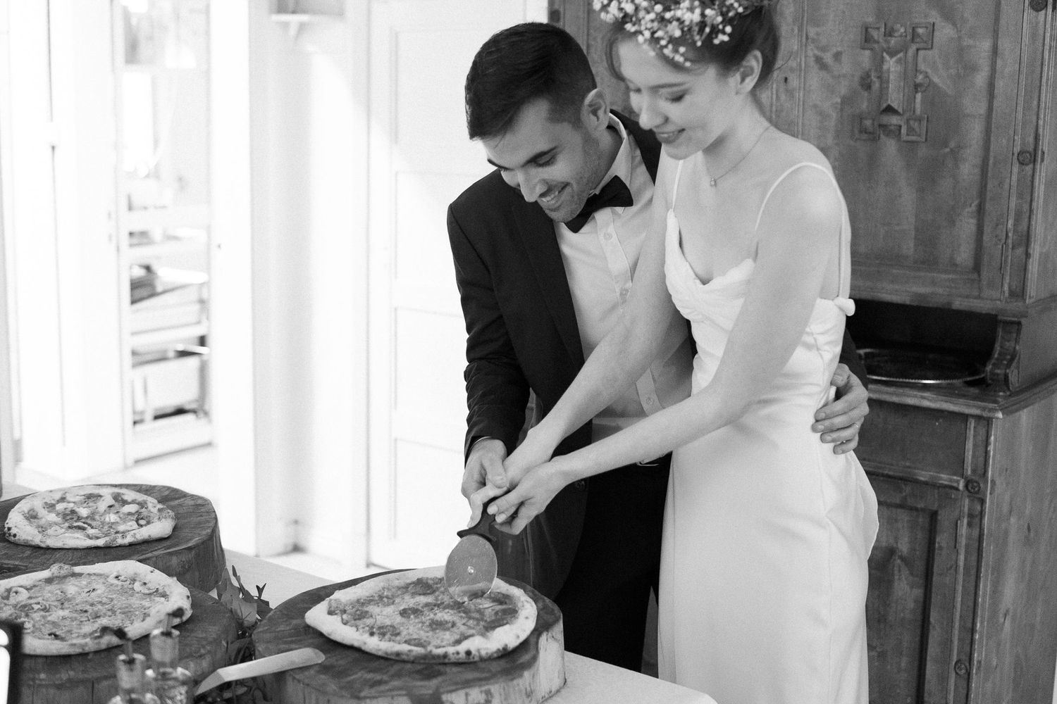 Wedding guests enjoy a casual dining experience with pizzas being served at rustic wooden tables.