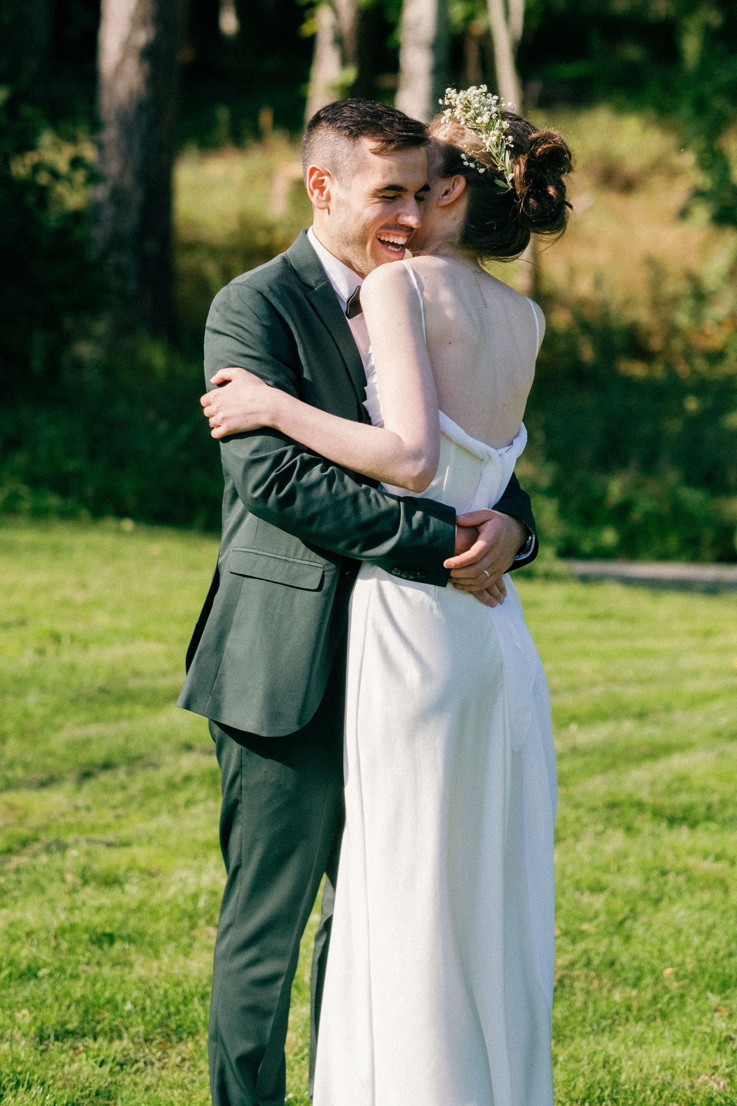 A happy couple embraces on their wedding day in a sunlit garden with trees in the background.