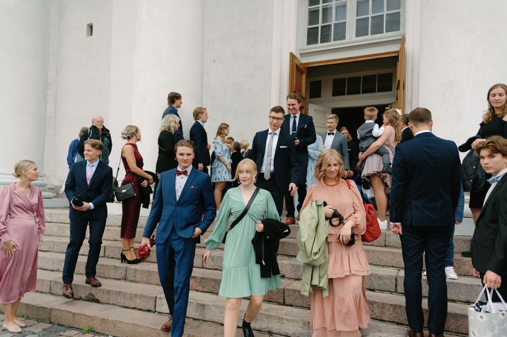 Wedding guests gathered on white stone steps outside a grand building.