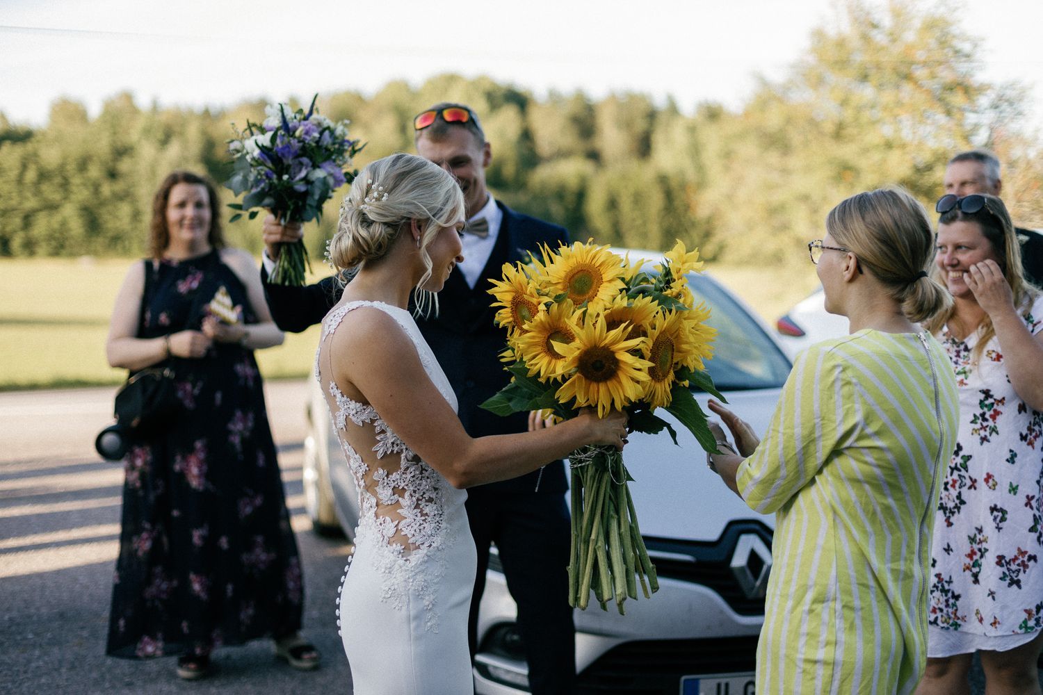 Wedding guests and sunflowers visible in outdoor celebration setting.