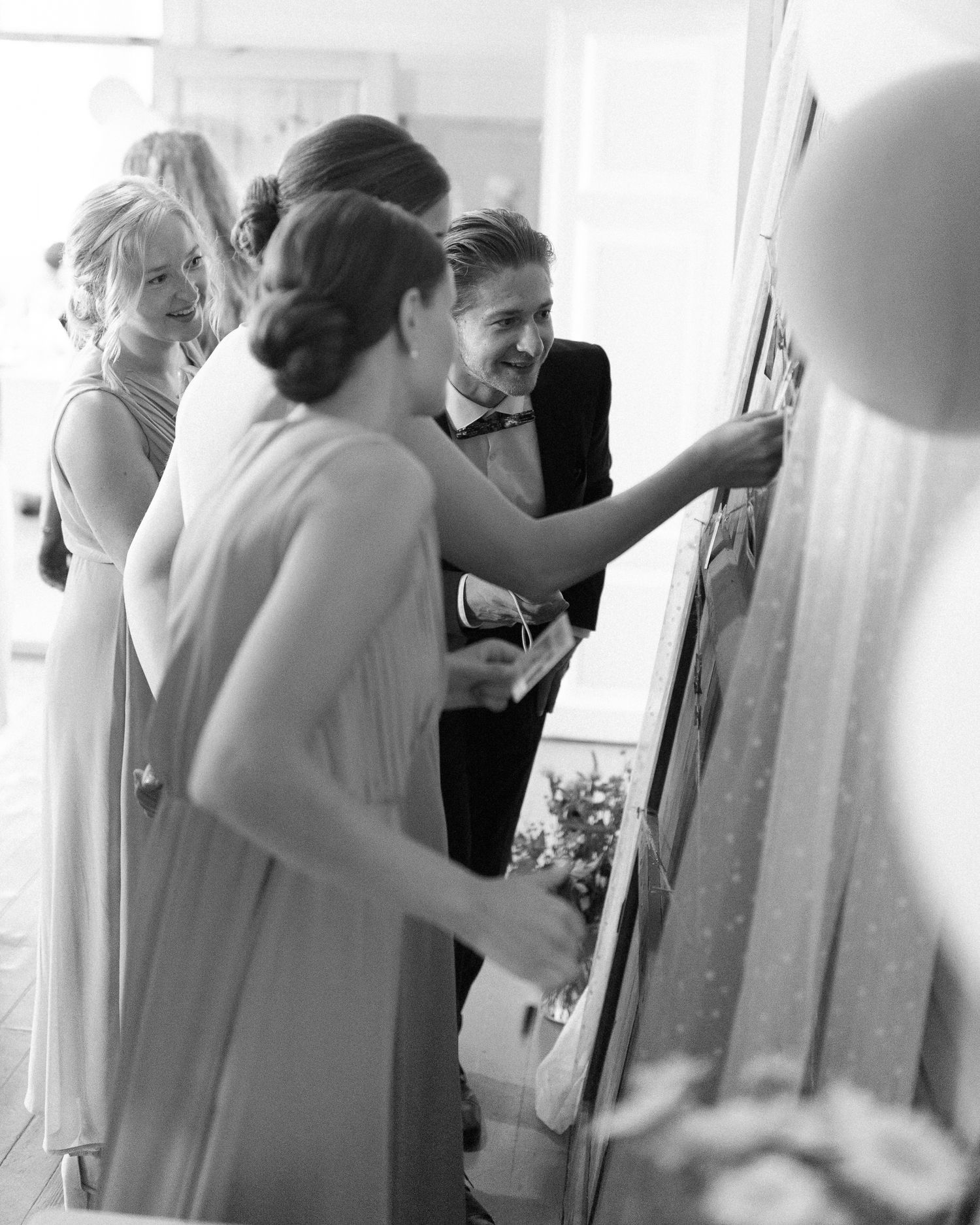 Wedding guests gathered around looking at something on the wall during reception.