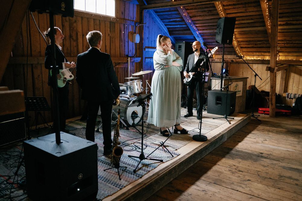 Wedding band performs on wooden stage in rustic barn venue with professional lighting setup.