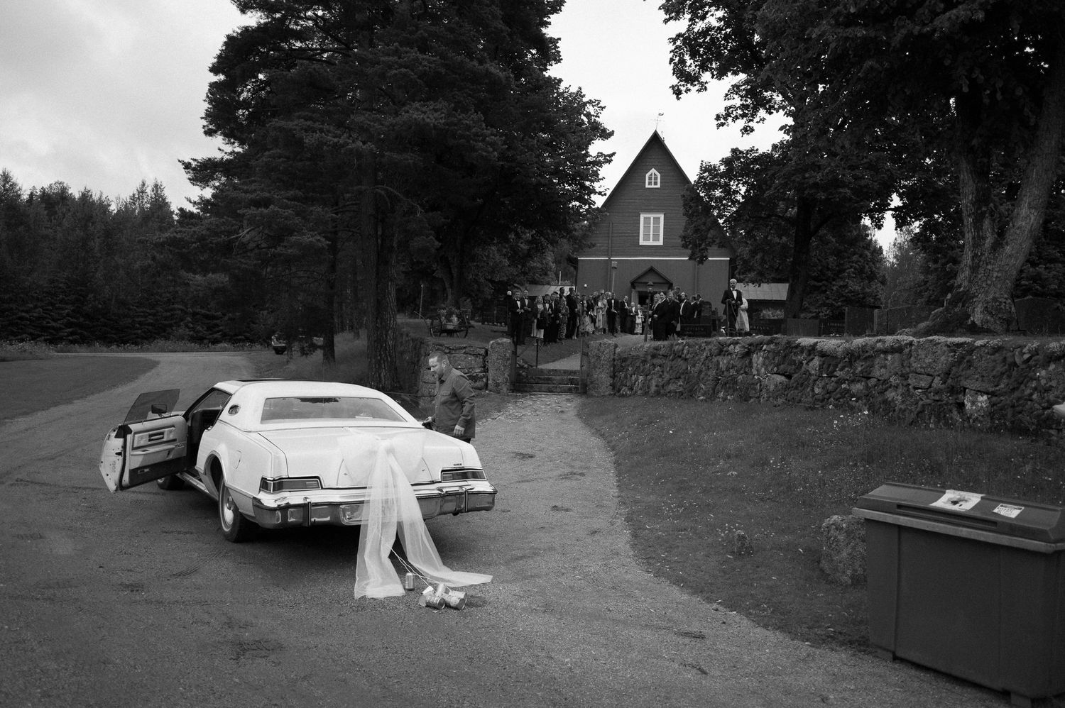Black and white photo of a vintage car parked near a rustic building.