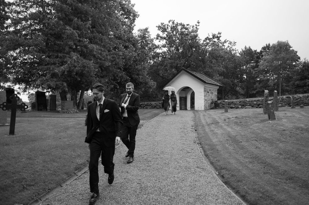 Wedding guests walk across a grassy lawn towards a small white chapel in the distance.