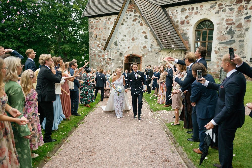 Wedding party walks down church path while guests shower them with white confetti.