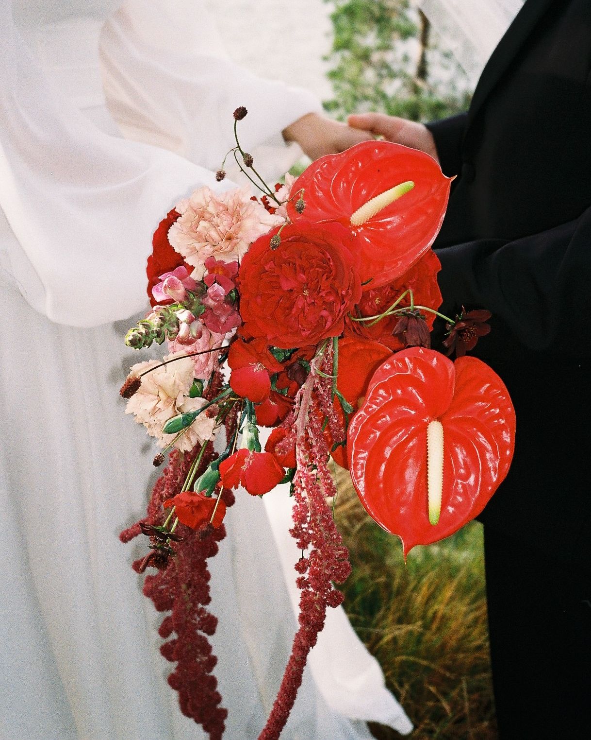 Red anthurium flowers and pink blooms in wedding bouquet against white dress.