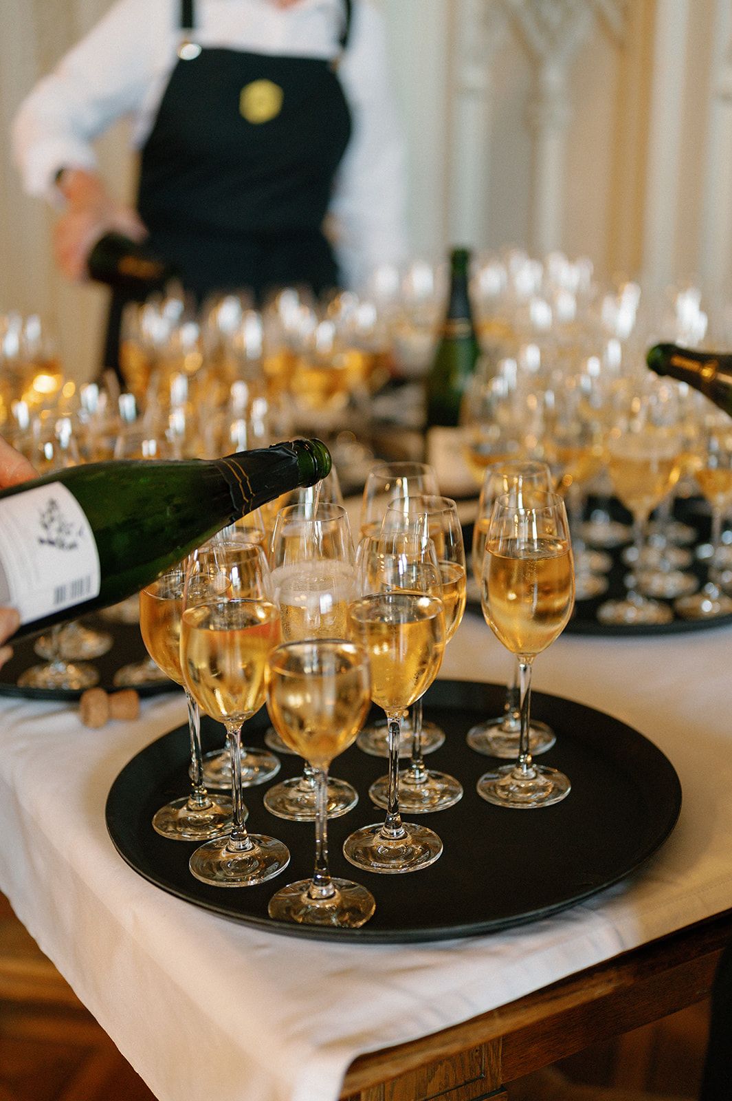 Multiple champagne glasses filled with golden liquid on black serving platters.