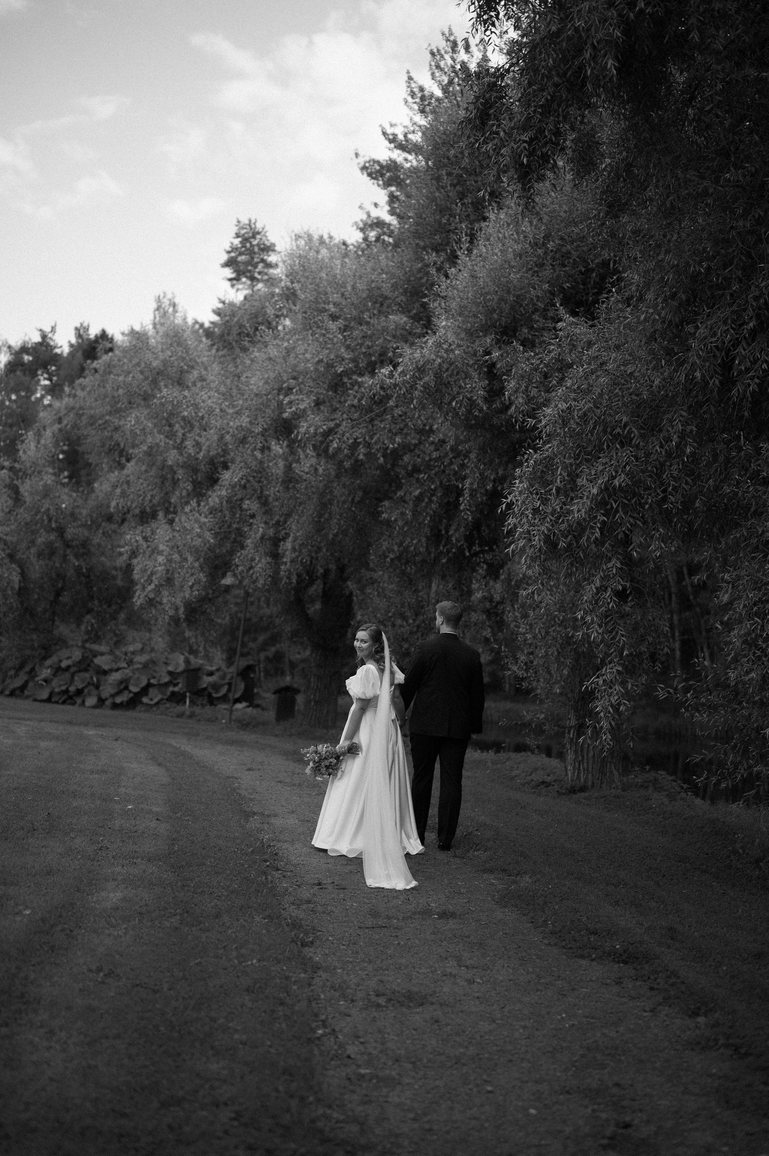 Distant black and white shot of wedding couple walking through a natural landscape.
