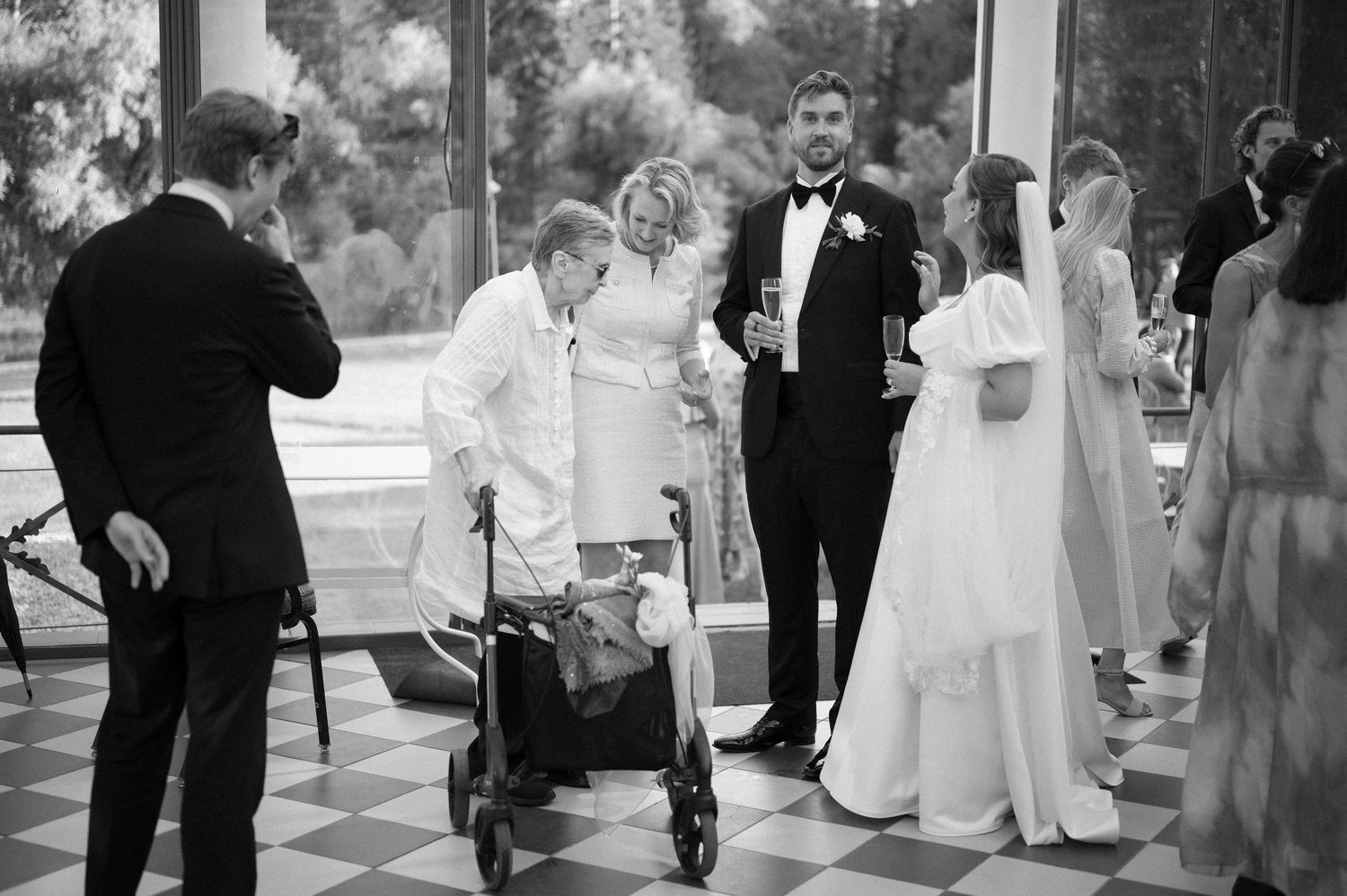 Black and white photo of guests gathered during an indoor wedding celebration.