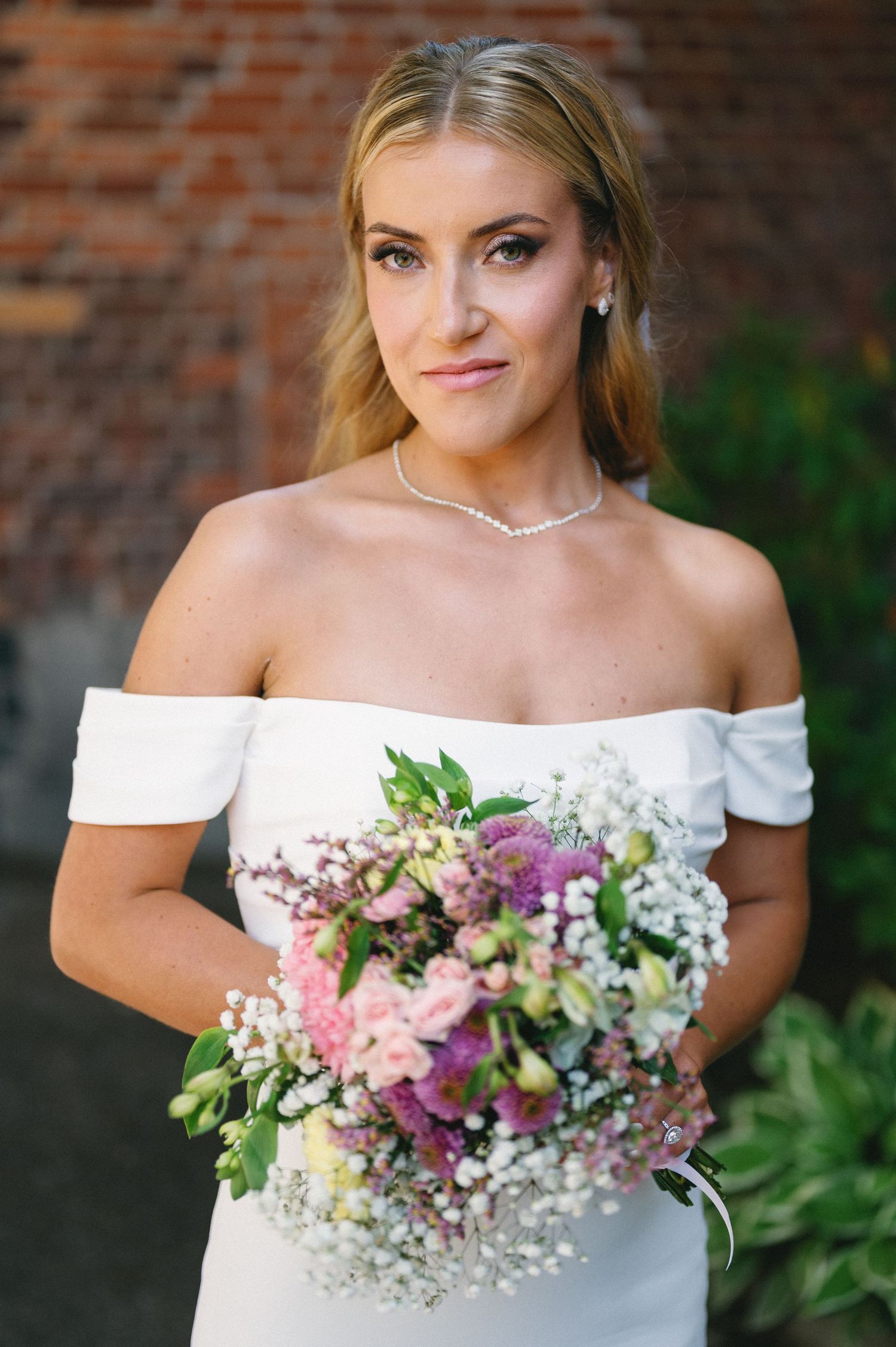Bridal portrait featuring an off-shoulder white gown and colorful mixed floral bouquet.