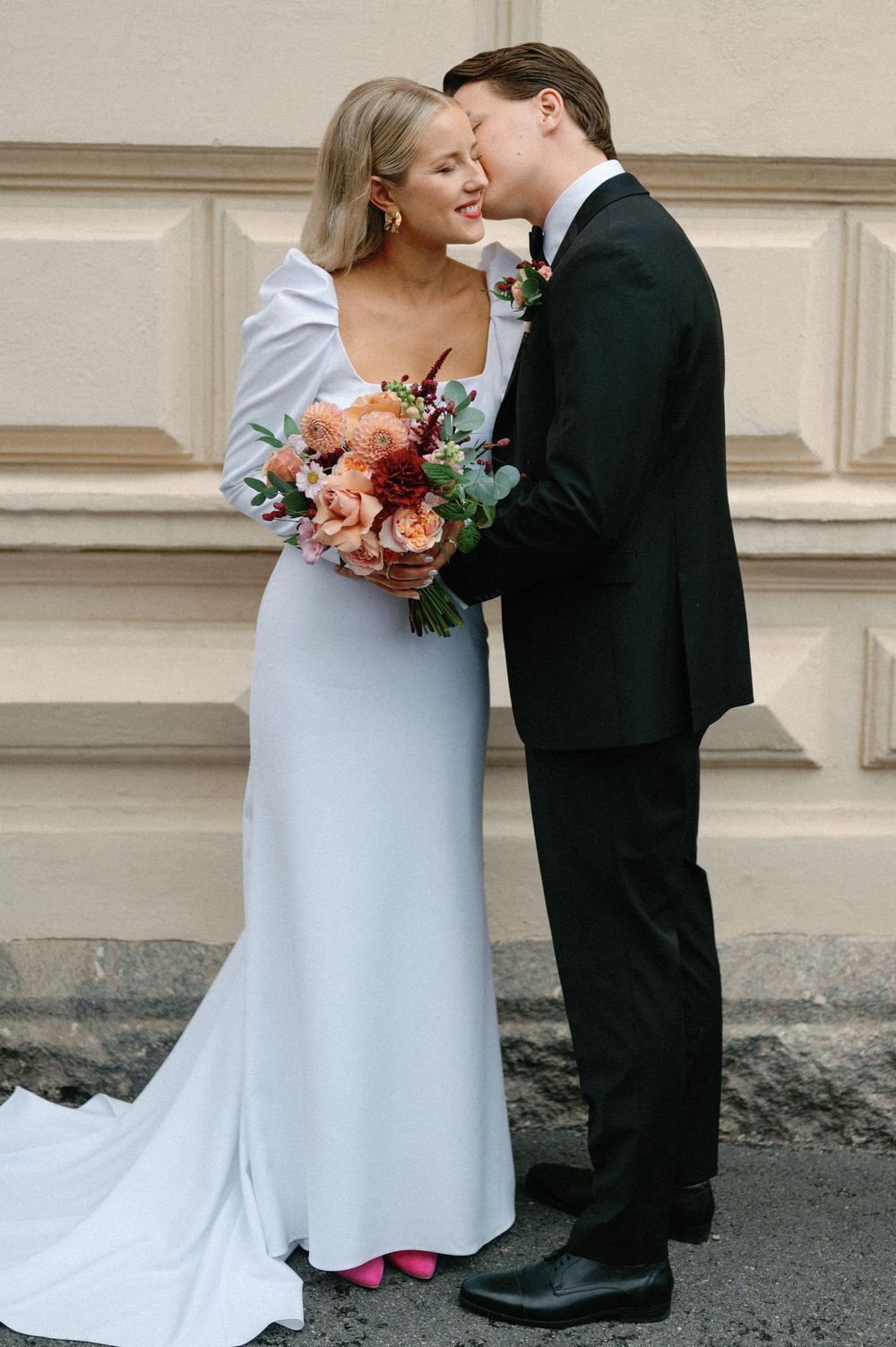 Wedding couple in classic attire sharing intimate moments against architectural backdrop.