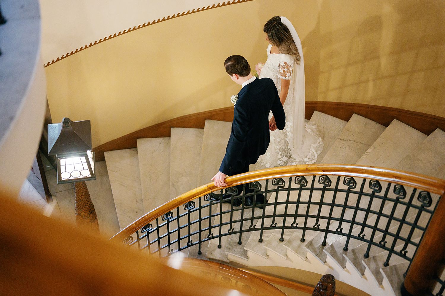 Wedding couple descending an elegant curved staircase with ornate railings.