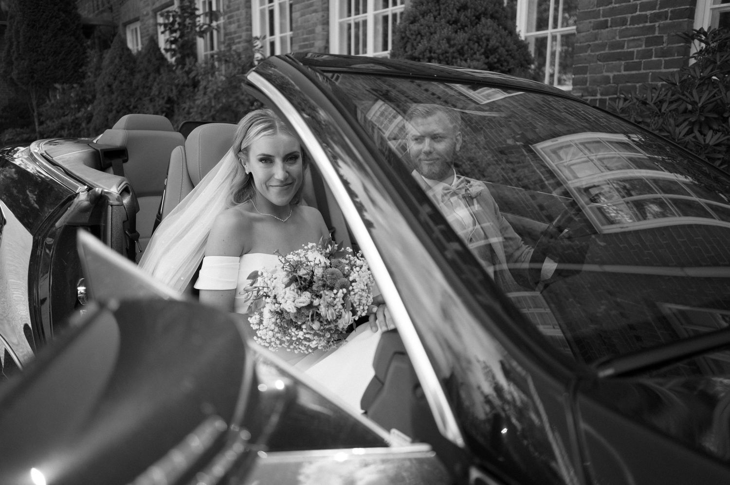 Wedding couple entering a black vehicle with bride's dress flowing behind.
