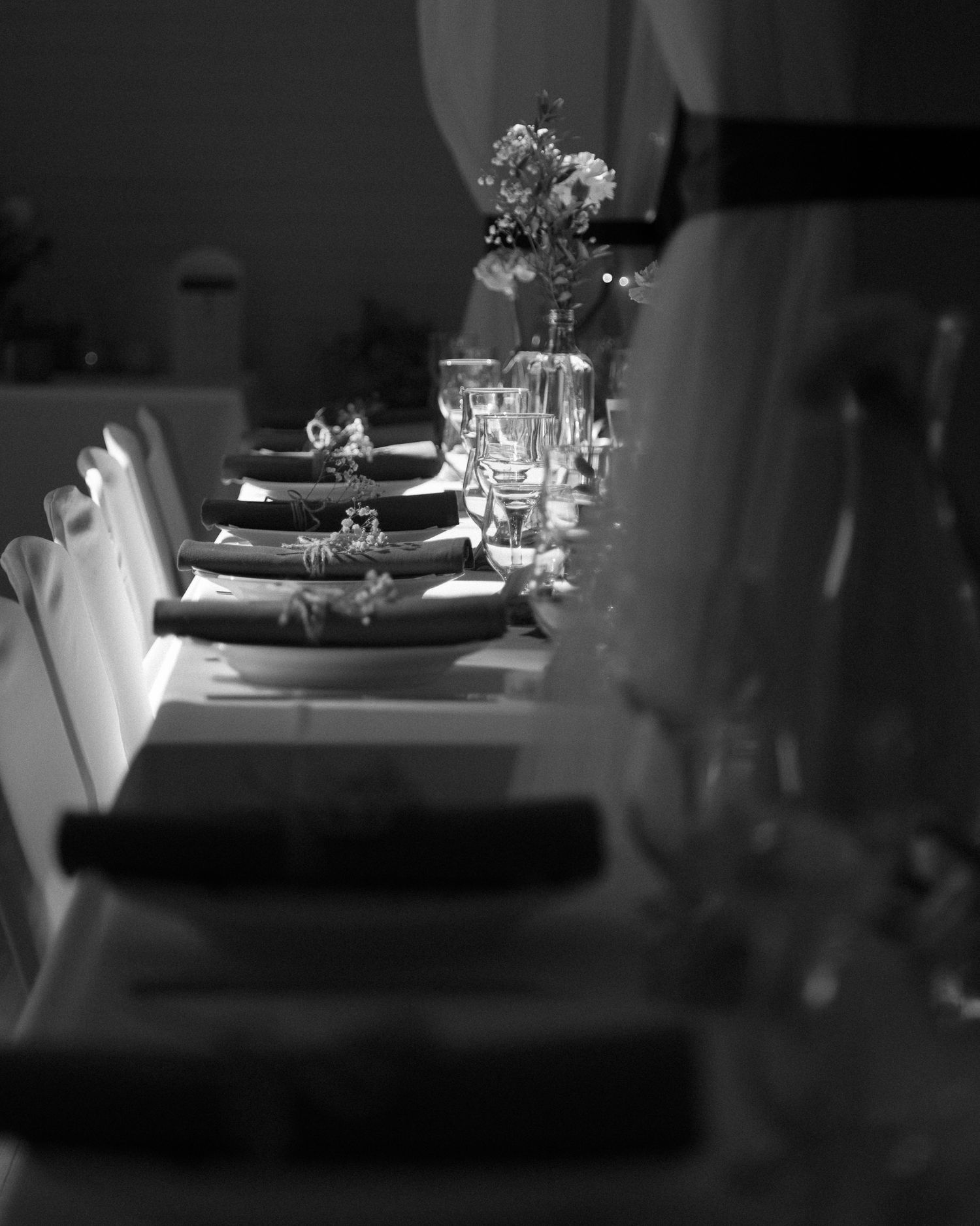 Black and white photo of formal place settings with delicate floral centerpieces on a long dining table.