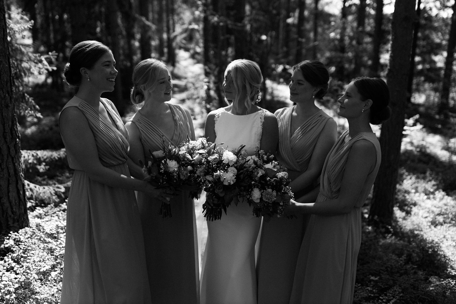 Black and white photo of wedding party members embracing in a forest.