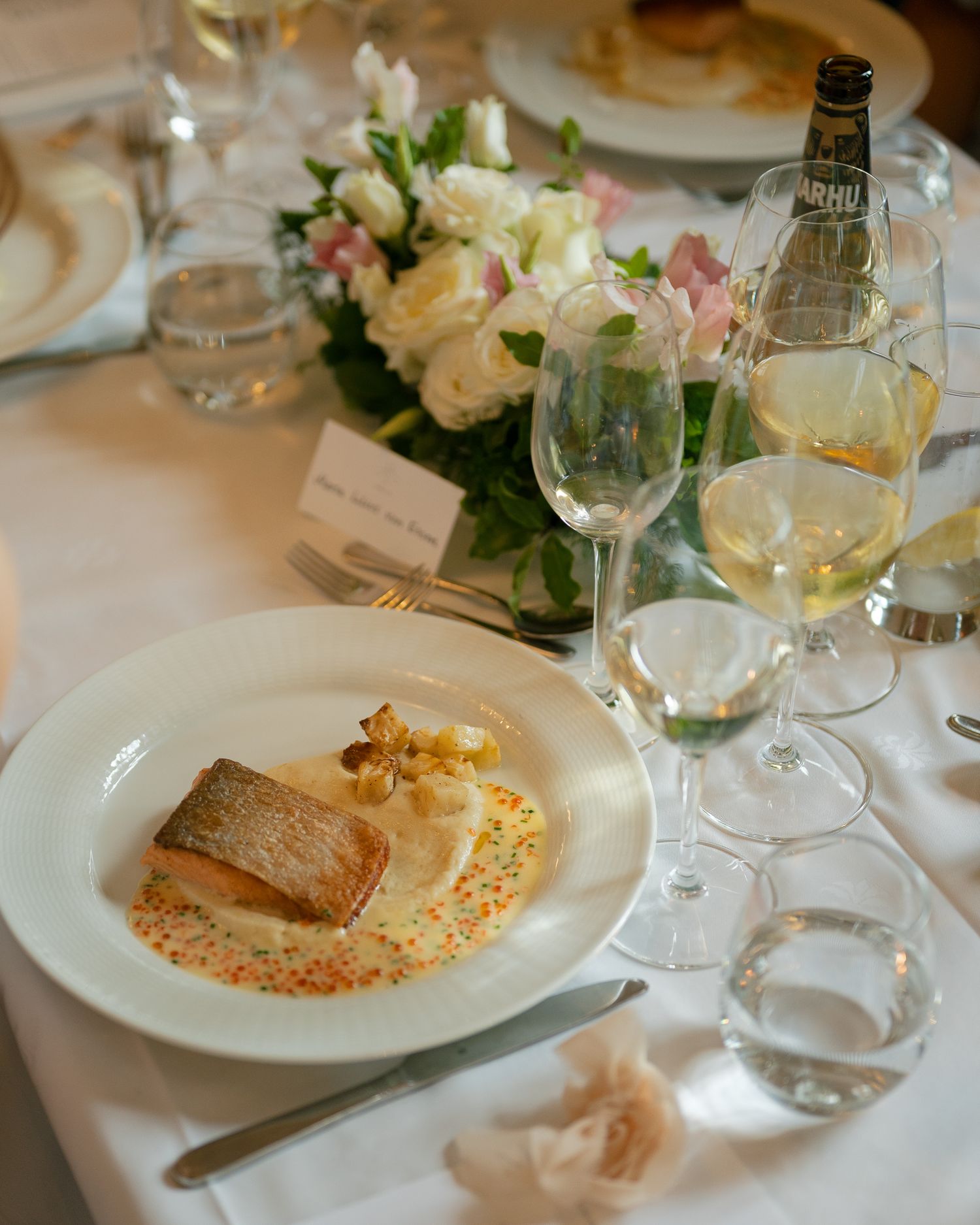 Elegant table setting with salmon dish, wine glasses, and white floral centerpiece at upscale restaurant.