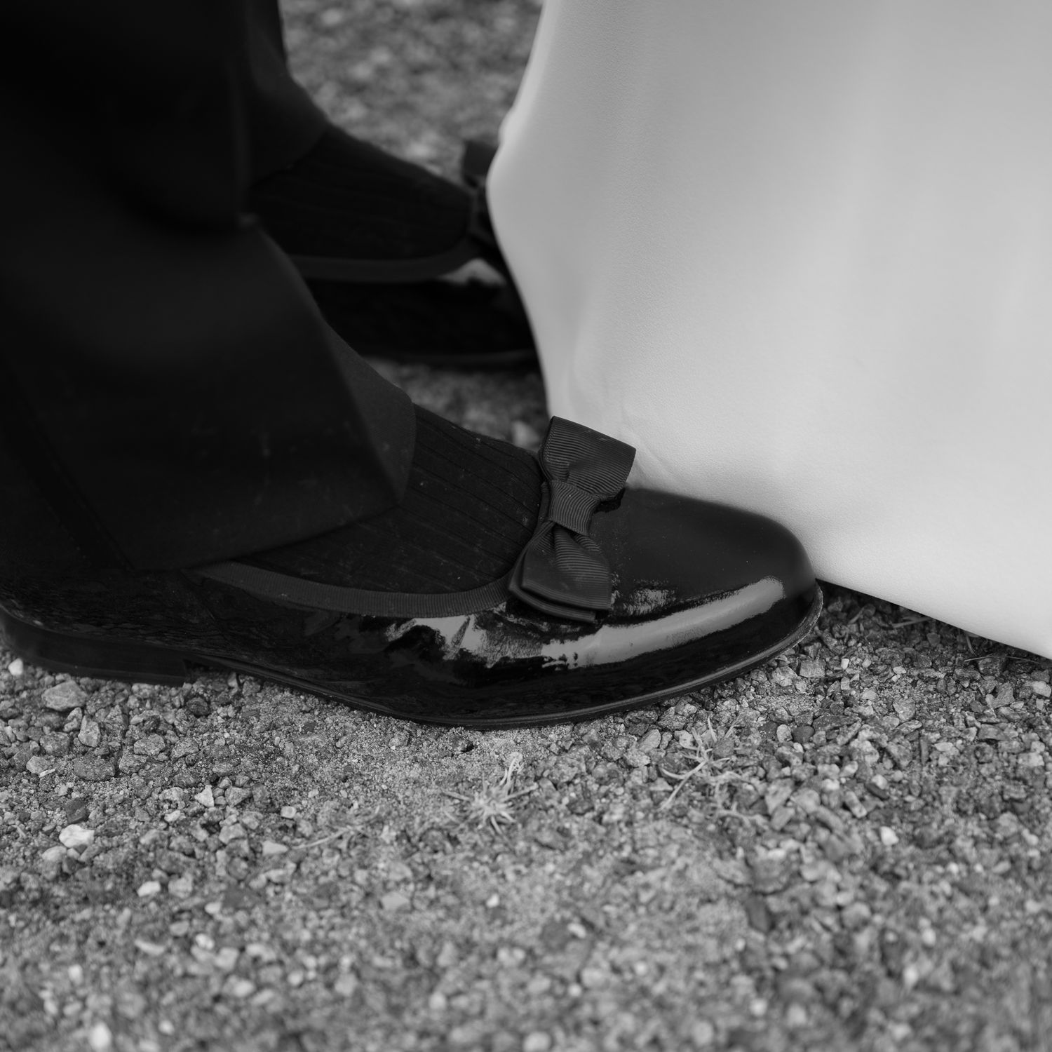 Close-up black and white photo of dress shoes and feet walking on a textured surface.