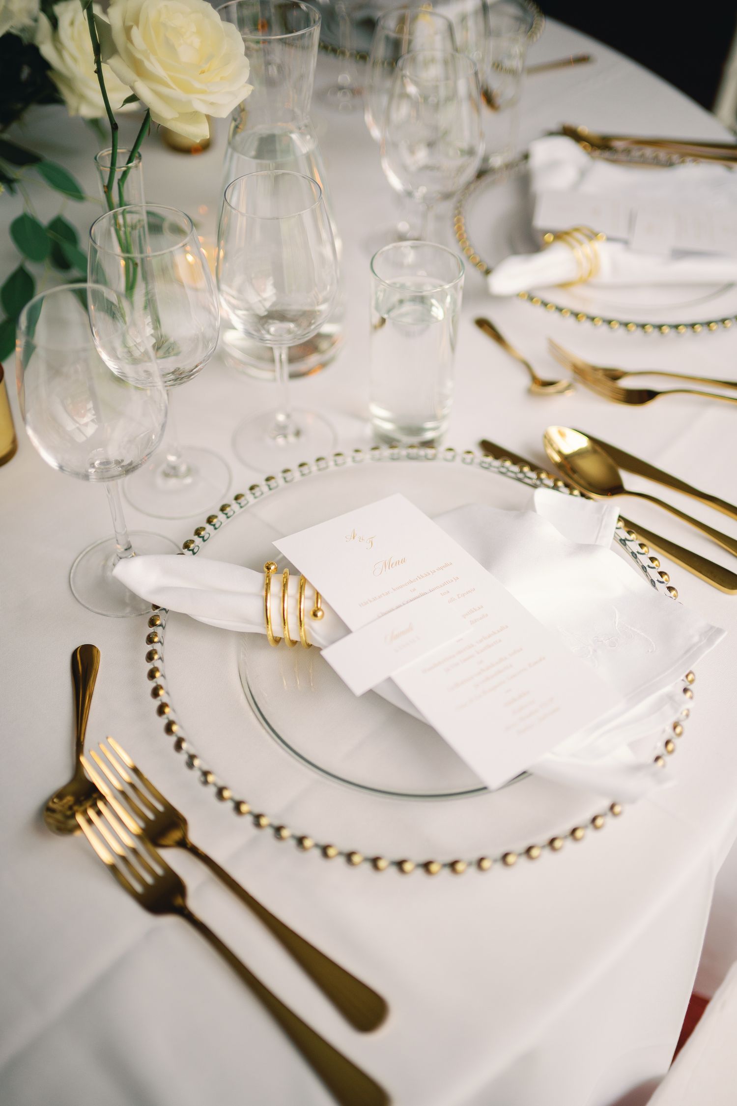 Elegant wedding table setting with gold cutlery, beaded charger plates, white napkins, menu cards, and crystal glassware.