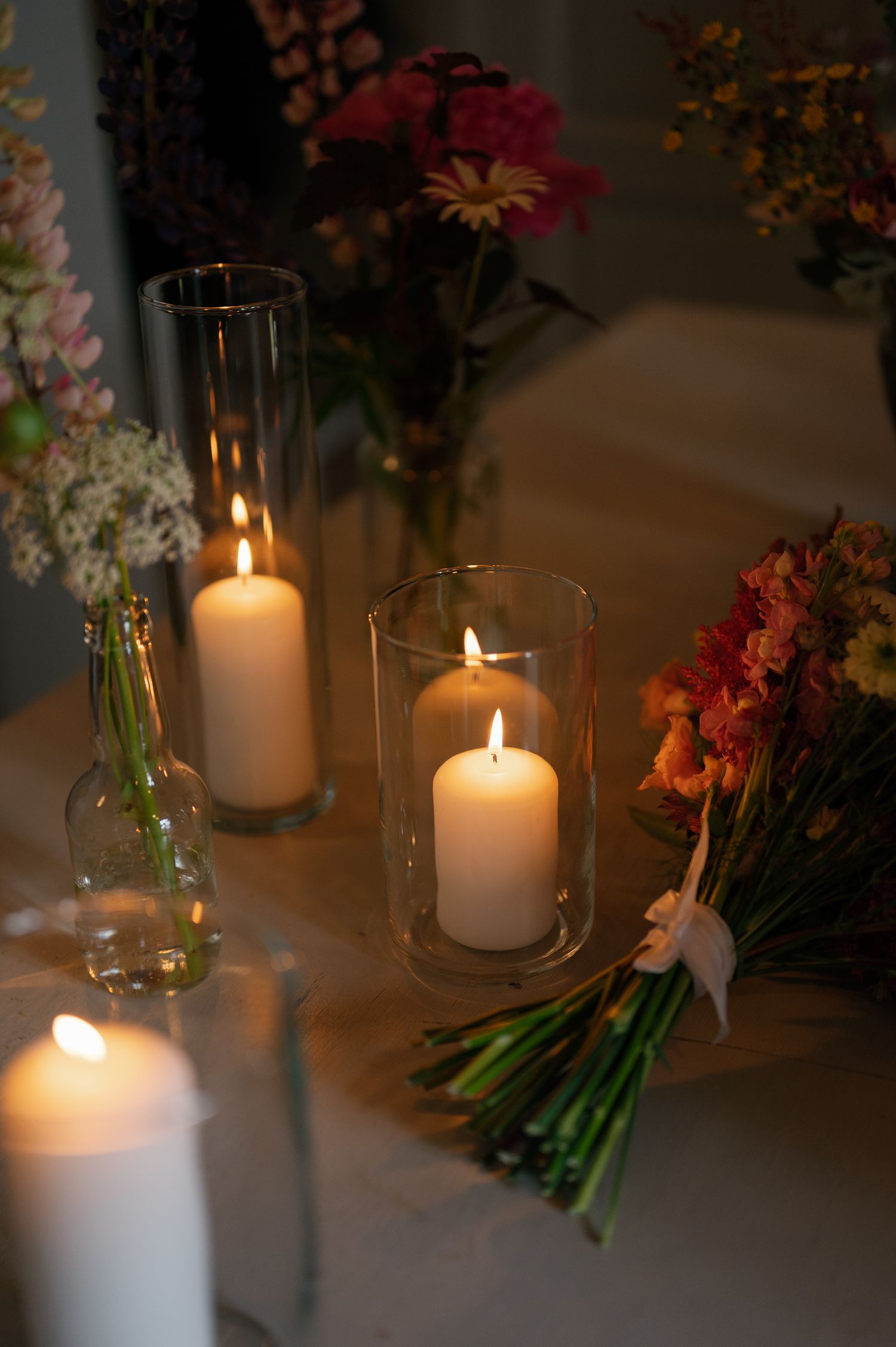 Table decorations featuring white candles in glass holders surrounded by fresh flower arrangements.