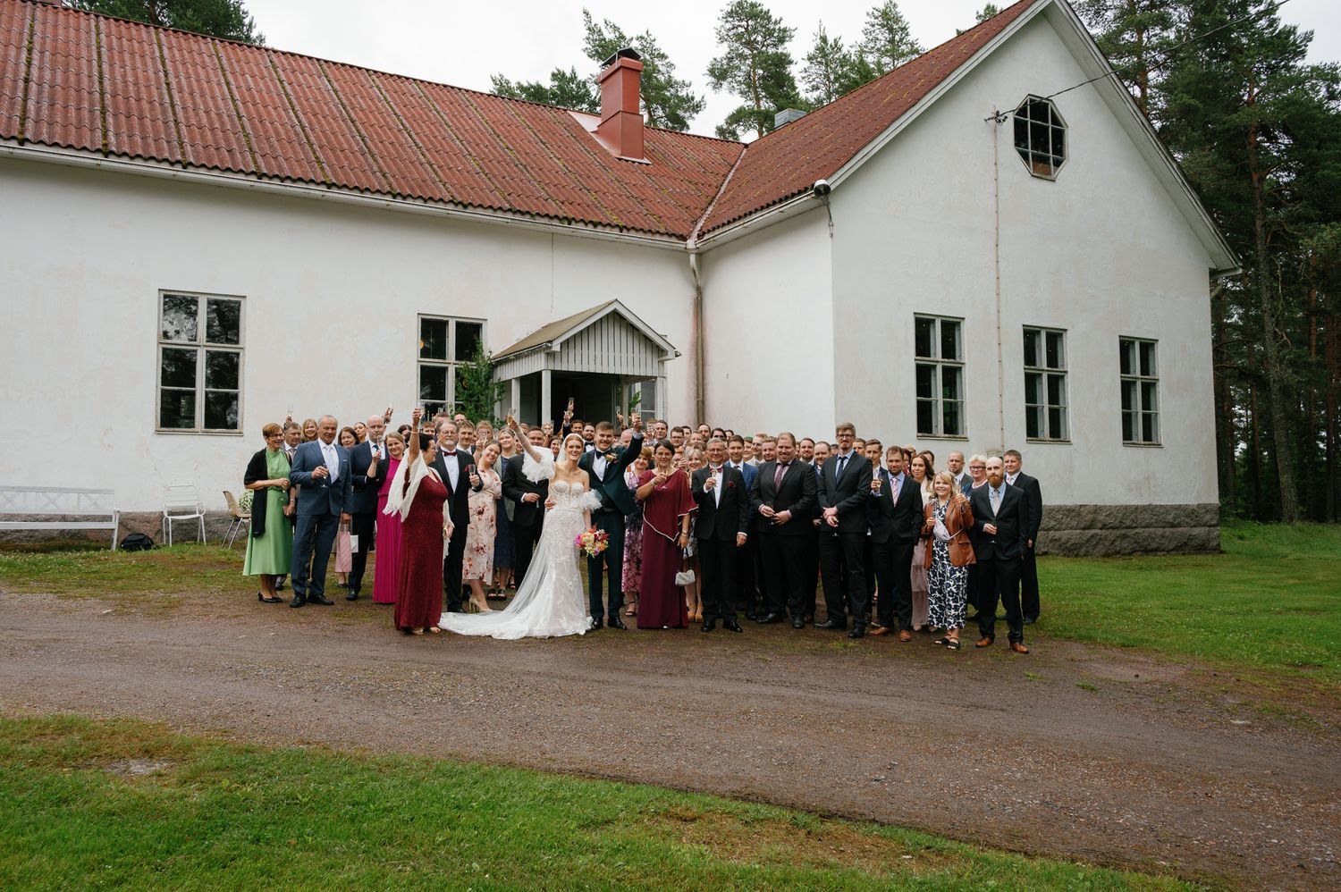 White countryside church building with red roof and wedding guests gathered outside.