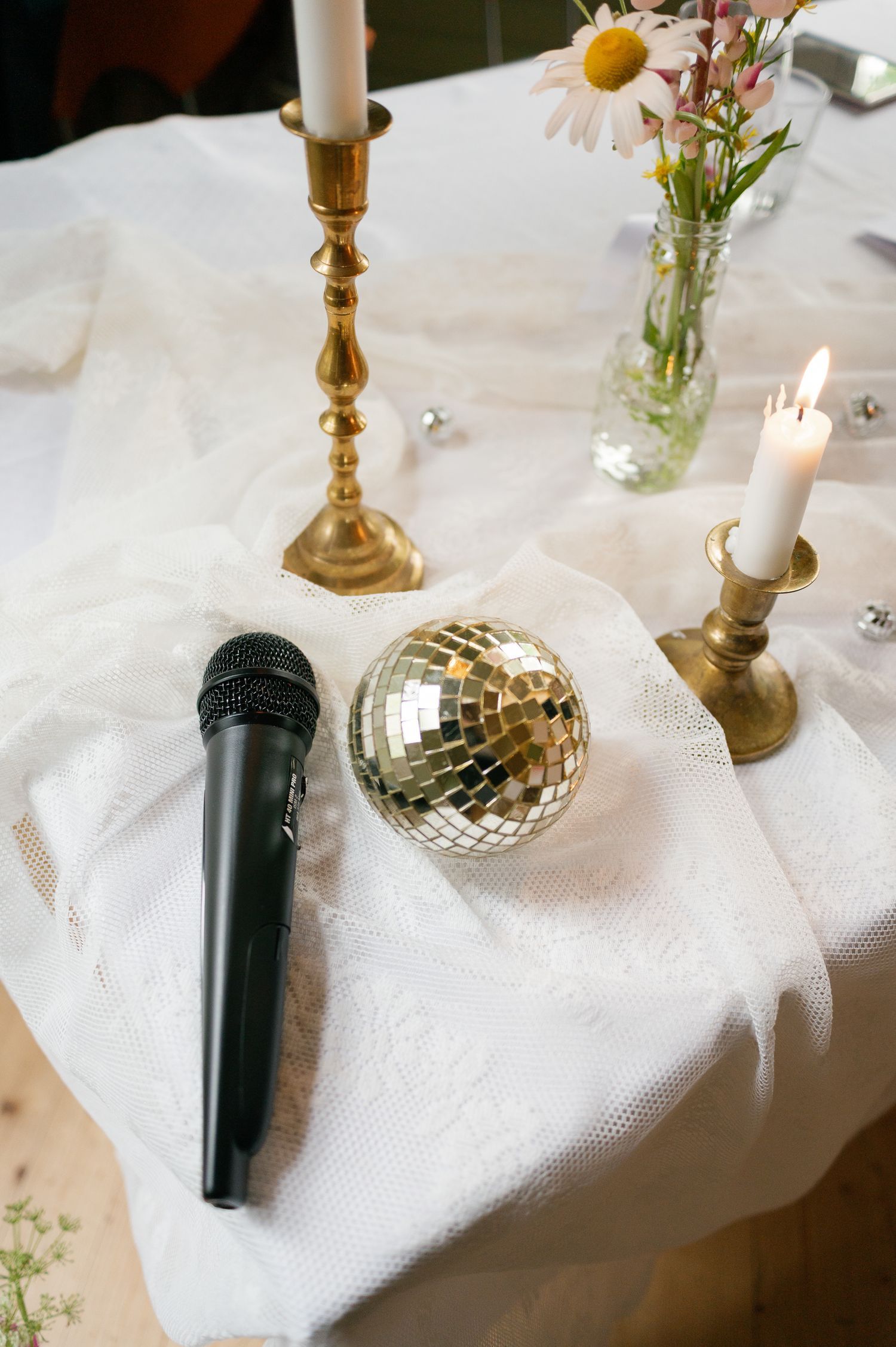 Table decor featuring brass candlesticks, a disco ball, and microphone on white linens.