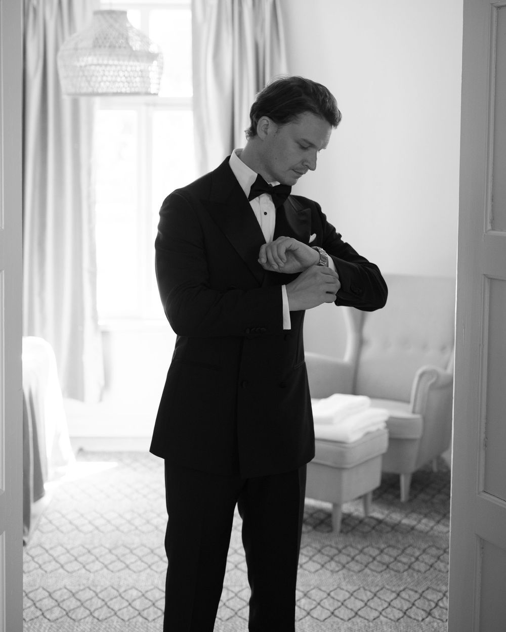 Person in black tuxedo bending down to adjust something in bright room.